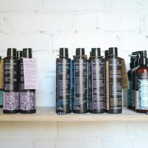A variety of natural cosmetic bottles lined up on a wooden shelf against a white brick wall, suggesting eco-friendly beauty.